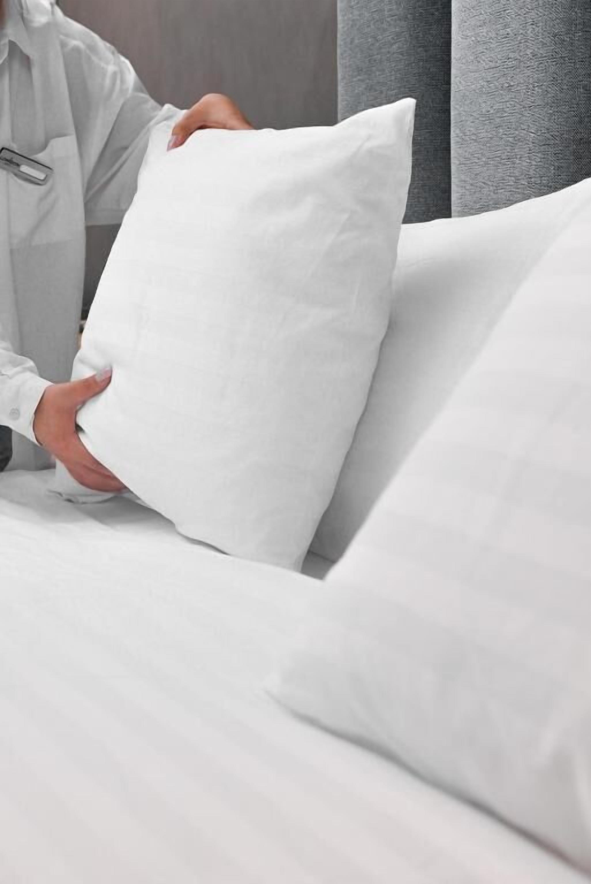 Una persona acomodando un almohadón blanco sobre la cama.