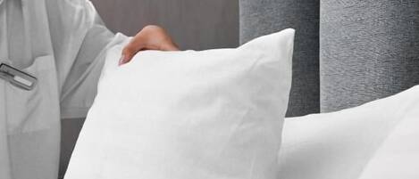 Una persona acomodando un almohadón blanco sobre la cama.