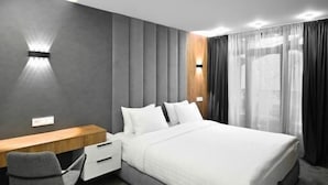 Ett modernt hotellrum med en stor säng, ett skrivbord med en stol och en väggmonterad lampa.