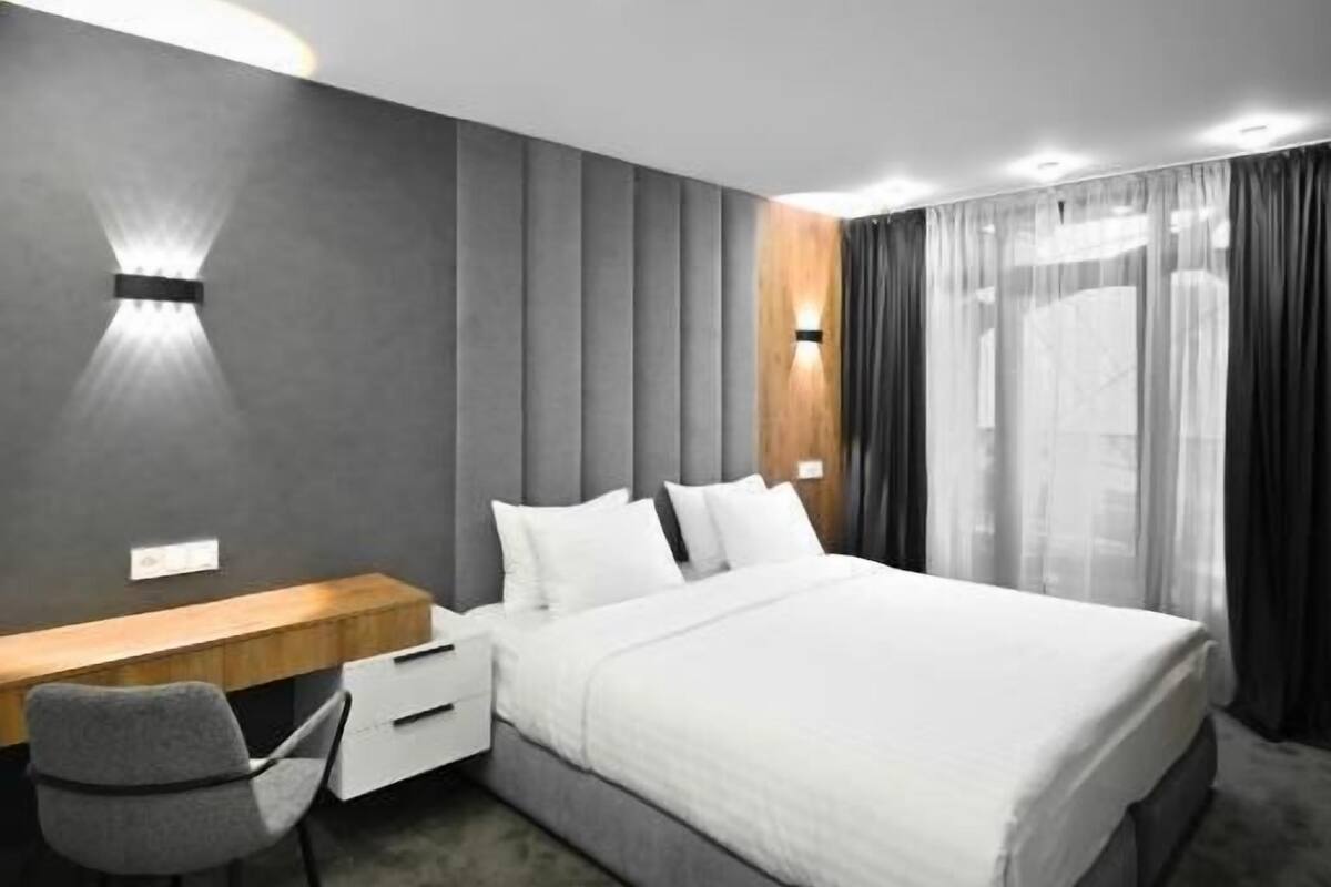 Ein modernes Hotelzimmer mit einem großen Bett, einem Schreibtisch mit Stuhl und einer Wandleuchte.
