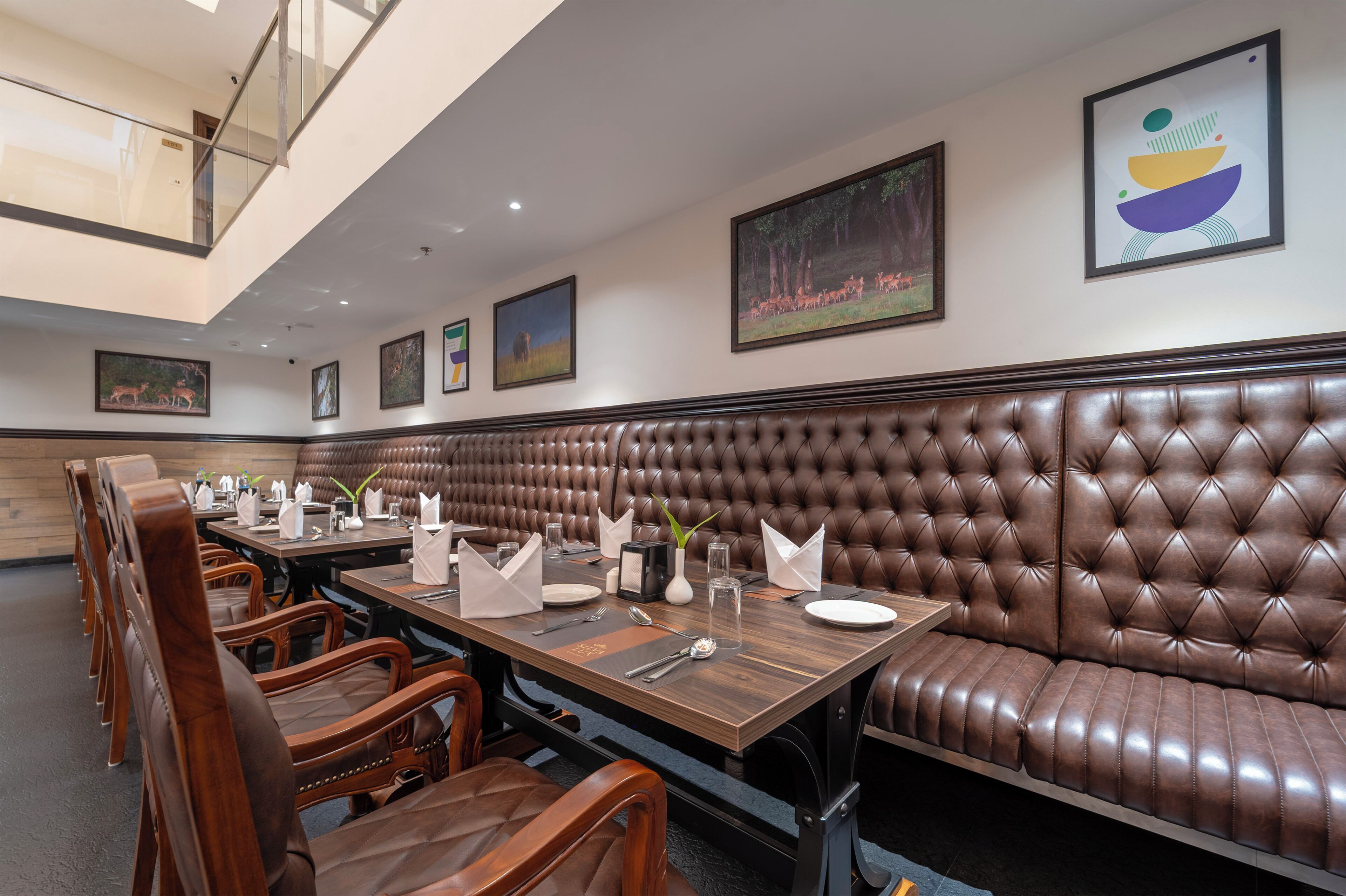 A restaurant with a long brown leather booth, wooden tables, and chairs.