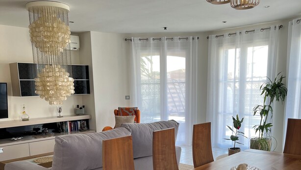 Un salon moderne avec une table à manger en bois, des sièges confortables, un lustre et un téléviseur fixé sur un meuble mural.