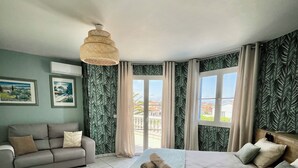 Une chambre avec un lit, un canapé, un luminaire en rotin et une vue par la fenêtre.