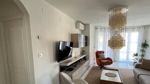 Un salon moderne avec un téléviseur à écran plat, un canapé, une table basse et un lustre.