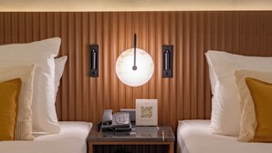 Habitación de hotel con dos camas, una mesita de noche con teléfono y un cartel con código QR, y un aplique de pared.