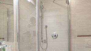 Ett modernt badrum med en duschavdelning med glasväggar, en vit tvättställ och en tvättställsbänk i trä.
