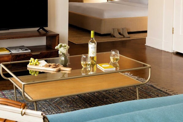 A modern living room with a glass-top coffee table, a book, a bottle of wine, and a vase with flowers.