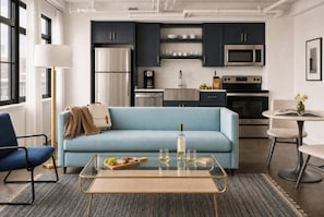 Une cuisine moderne avec des meubles de couleur sombre, des appareils en acier inoxydable et un canapé bleu clair dans l’espace salon.
