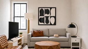 Ein Wohnzimmer mit einer Couch, einem Couchtisch, einem Fernseher, einer Lampe und einem Gemälde an der Wand.
