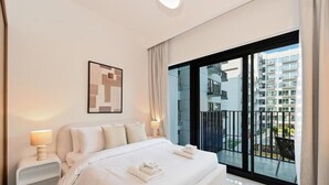 A modern hotel room with a large bed, a bedside table with a lamp, a framed artwork on the wall, and a balcony with a view of the city. - Bloomfields Sleek 1BR in Azizi Mirage 1 (Dubai)