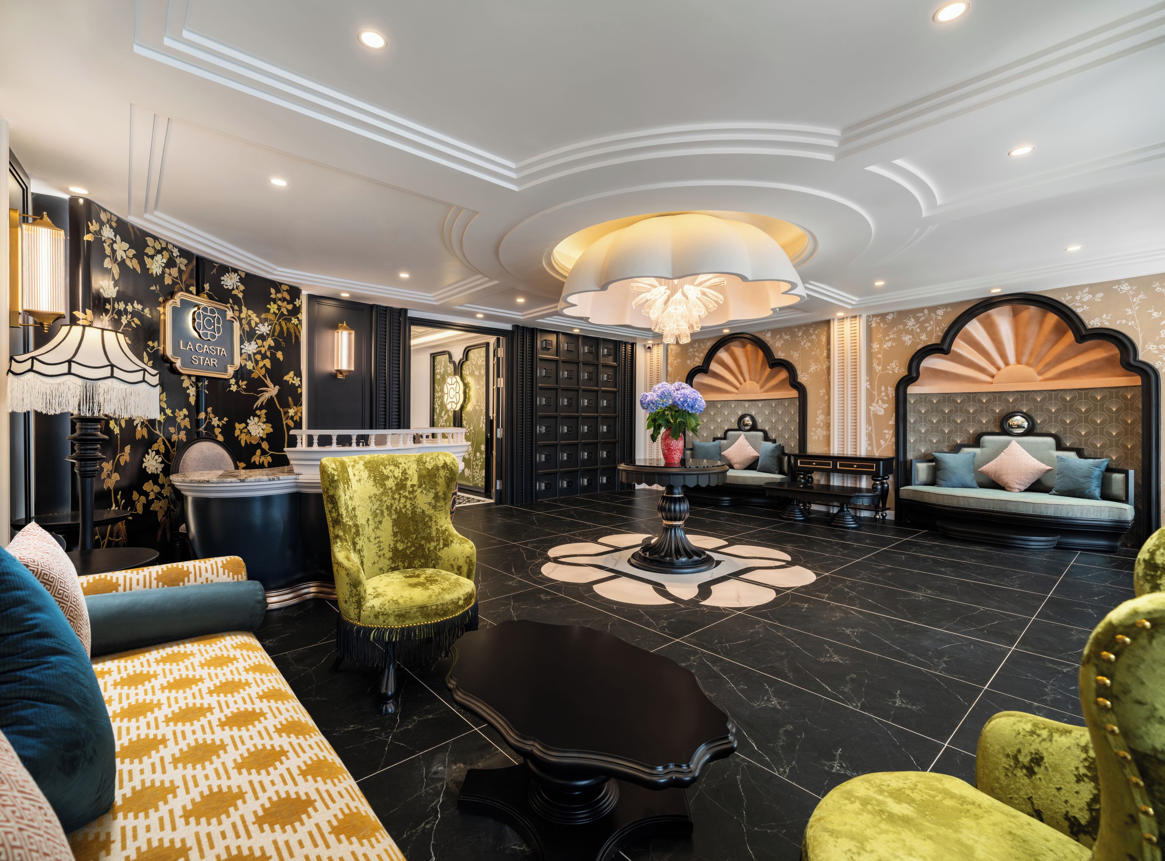 A luxurious lobby with a grand chandelier, plush seating, and a decorative wall with a floral pattern.