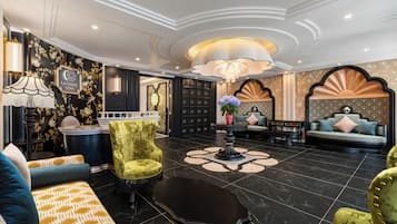 A luxurious lobby with a grand chandelier, plush seating, and a decorative wall with a floral pattern.