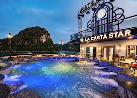 A waterfront hotel with a hot tub area, outdoor seating, and a mountain backdrop.