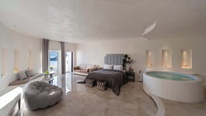 Un dormitorio moderno con una cama grande, un rincón de descanso, una bañera y vistas al exterior.