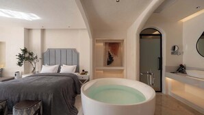 Un dormitorio moderno con una bañera grande, cama con ropa de cama gris y decoración minimalista.