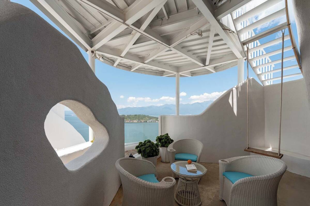 Un balcon moderne et ouvert, doté de meubles en osier et offrant une vue sur la mer.