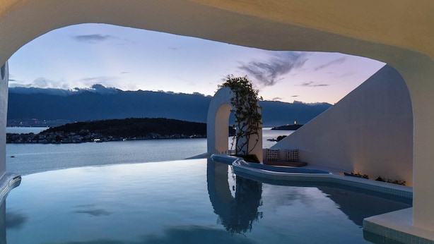 Una piscina infinita con una vista despejada del mar y montañas al fondo.