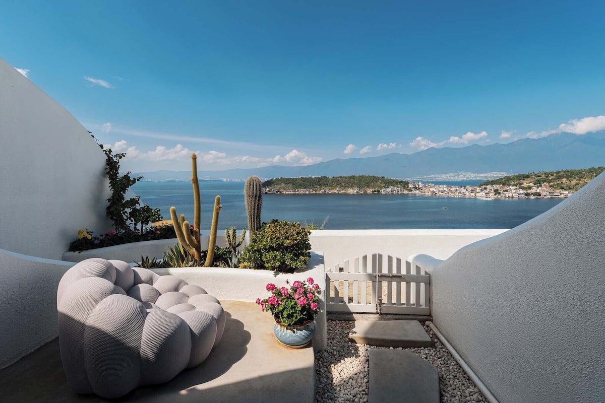 Un balcon avec une balustrade blanche, un cactus et une plante en pot ornée de fleurs roses.