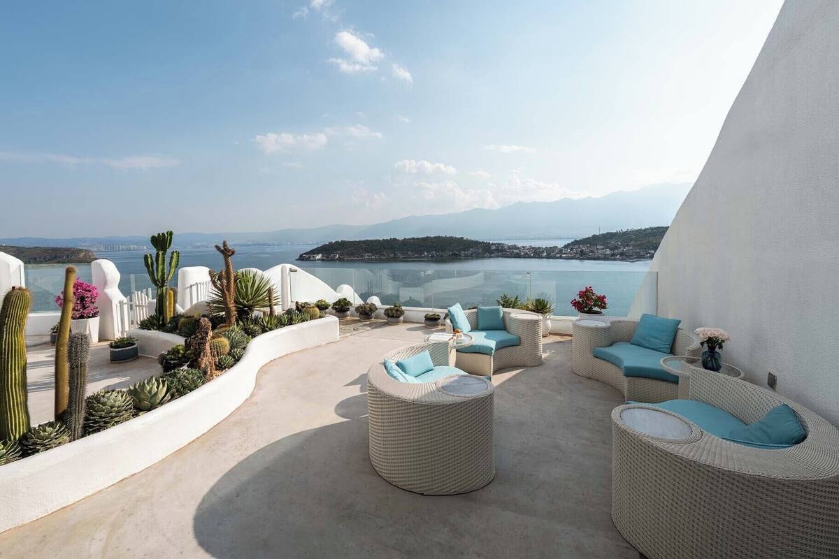 Une terrasse dotée de meubles en osier, de cactus et offrant une vue sur la mer et les montagnes.