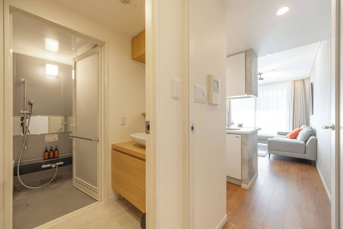 A modern bathroom with a shower, sink, and toilet. There is a small seating area with a sofa and a window.