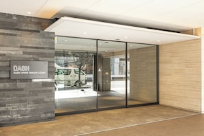 A modern building entrance with a glass door, a sign reading "DASH LIVING MINAMI AZABU", and a stone wall. - Dash Living Minami Azabu (Tokyo)