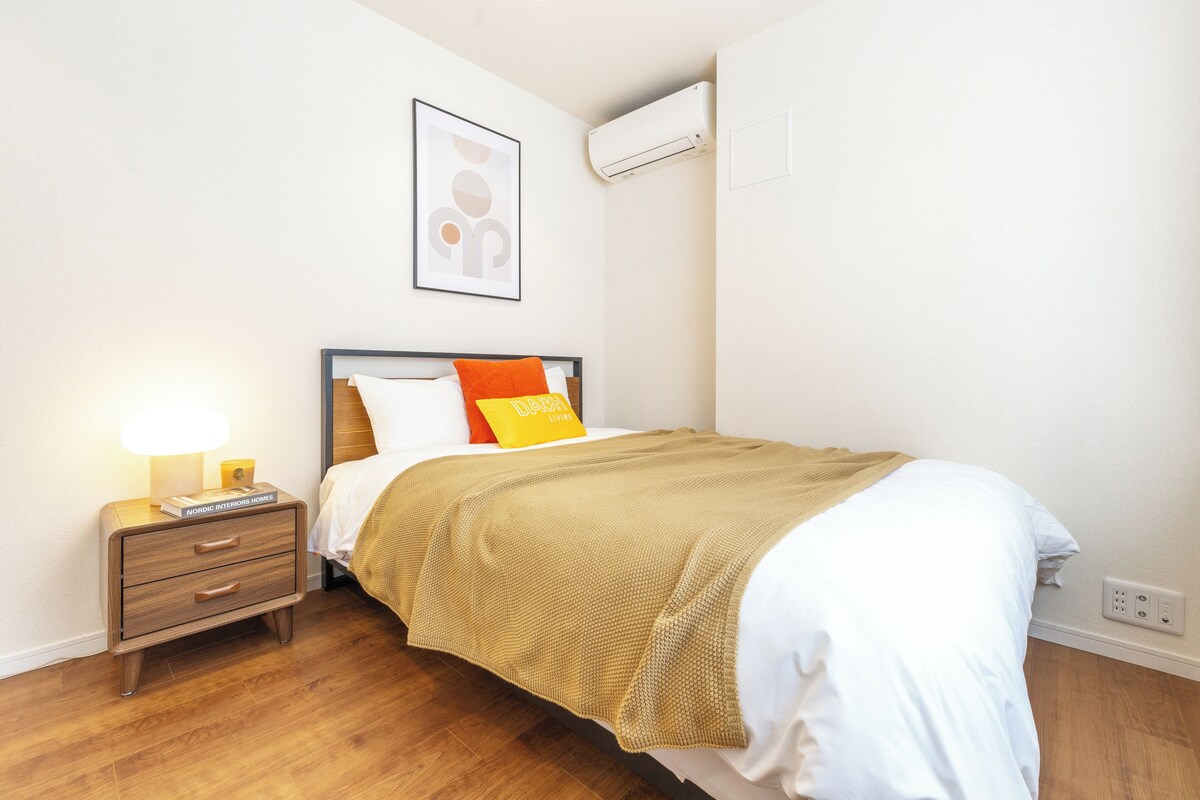 A neatly made bed with a headboard, a bedside table with a lamp, and a framed picture on the wall.