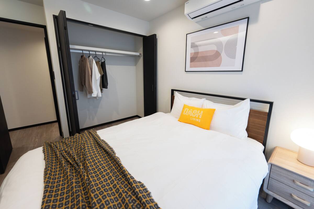 A hotel room with a bed, a bedside table, a nightstand, a wardrobe, and a framed picture on the wall.