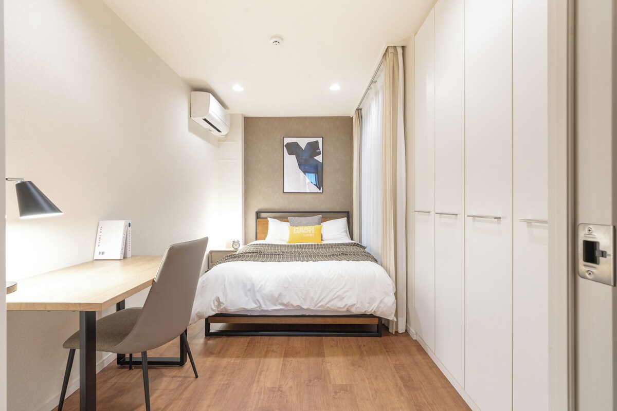 A bedroom with a bed, a desk, a chair, a wardrobe, and a wall-mounted air conditioner.
