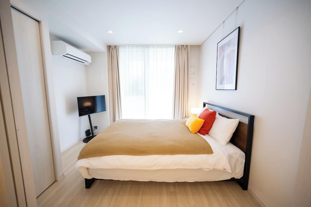 A modern hotel room with a large bed, an air conditioning unit, a flat-screen TV, and a window with curtains.