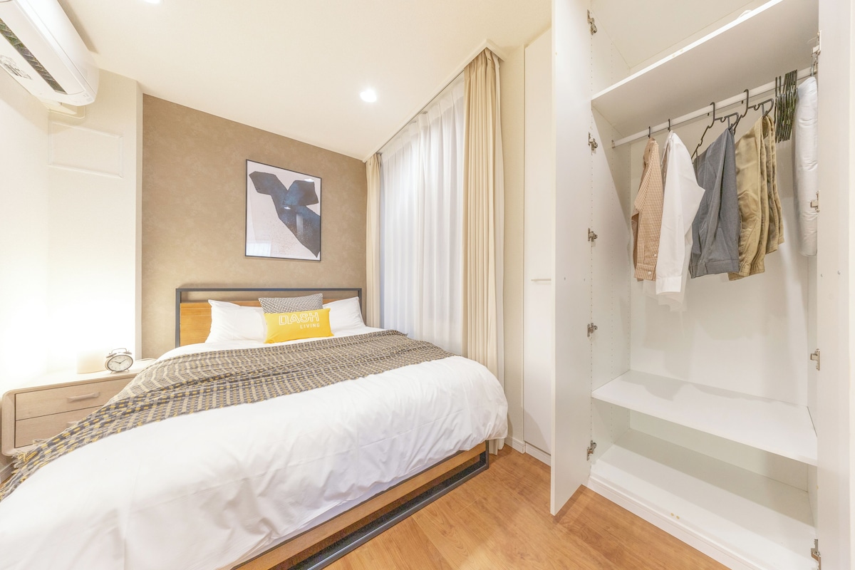 A bedroom with a bed, a bedside table, a nightstand, a wardrobe, and a wall-mounted air conditioner.