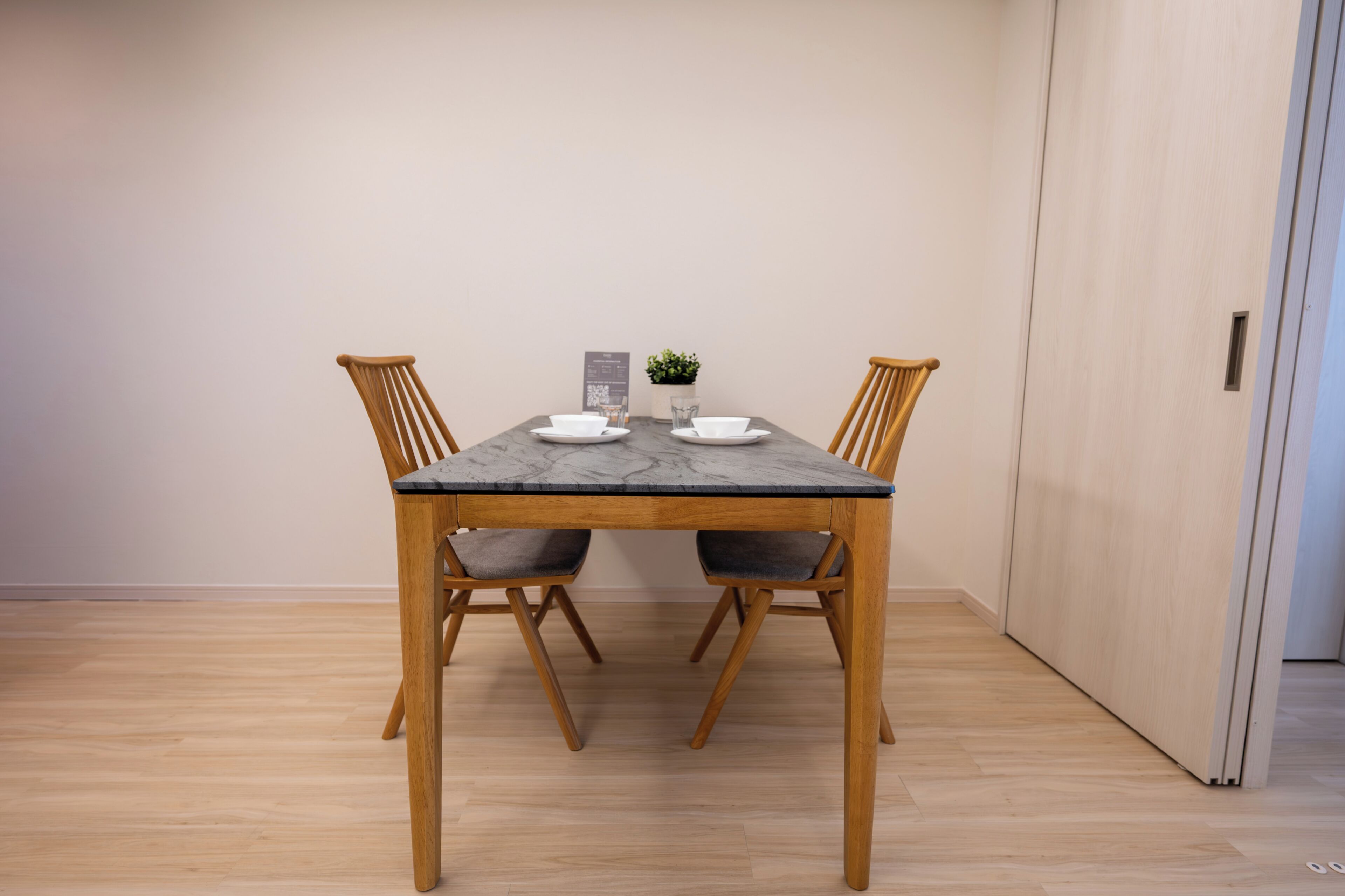 Una mesa de comedor con cuatro sillas, una planta pequeña en maceta y un atril para el menú.