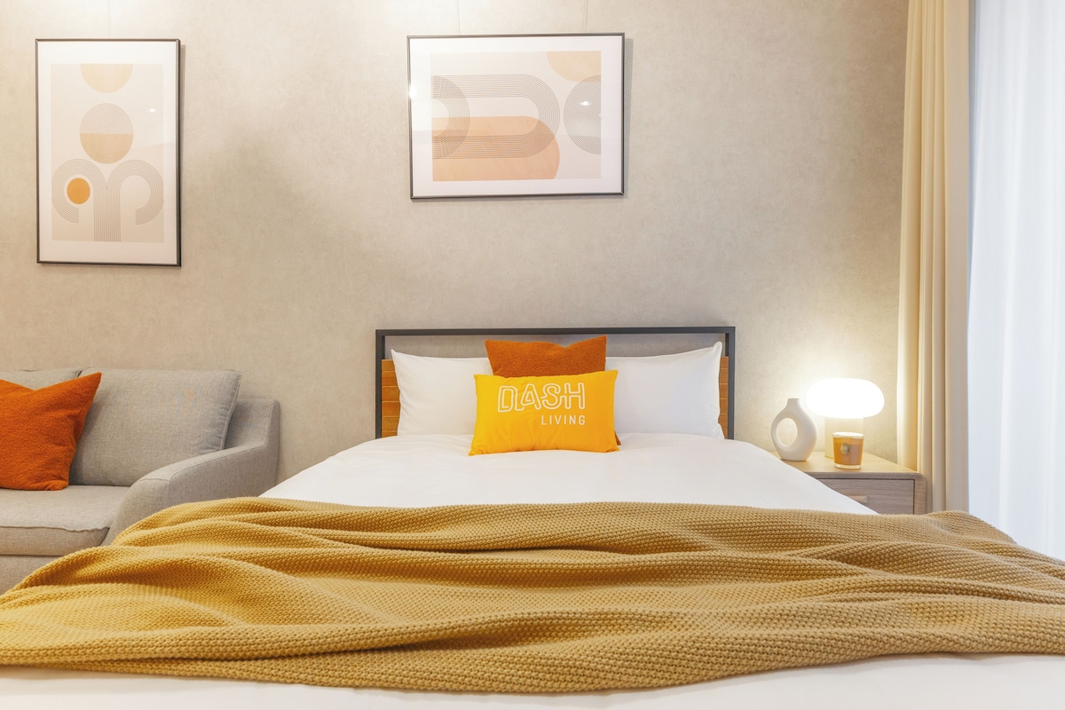 A hotel room with a bed, a nightstand, a lamp, and two framed artworks on the wall.