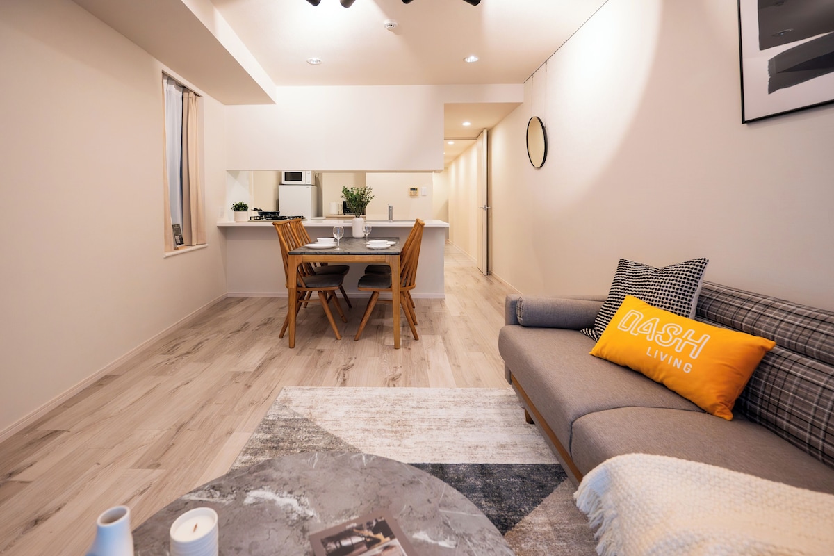 A modern apartment with a dining area, a sofa with a cushion, and a kitchen in the background.