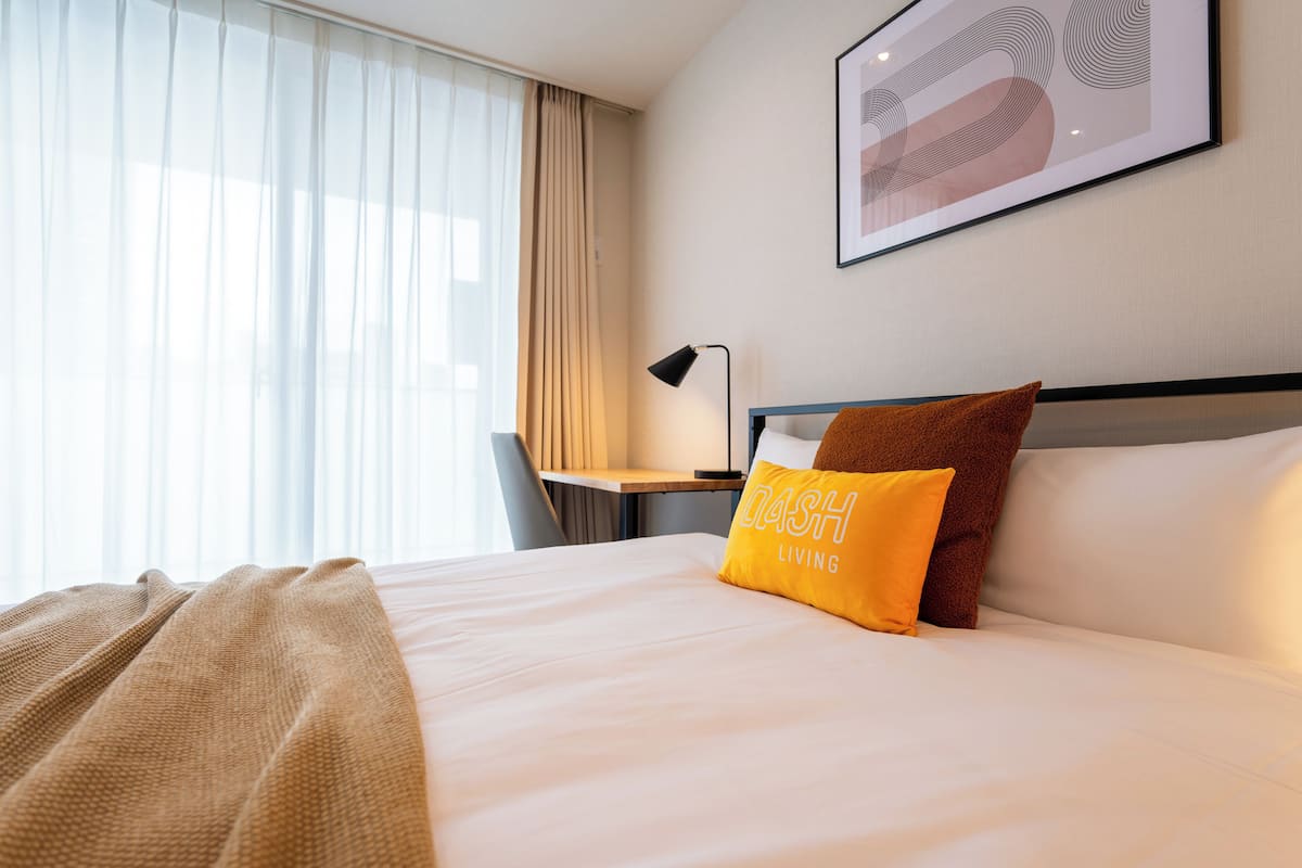 A hotel room with a bed, a desk, a chair, and a window with curtains.