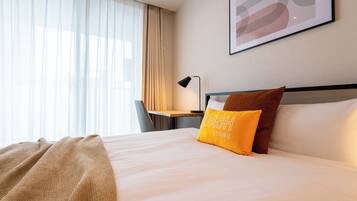 A hotel room with a bed, a desk, a chair, and a window with curtains.
