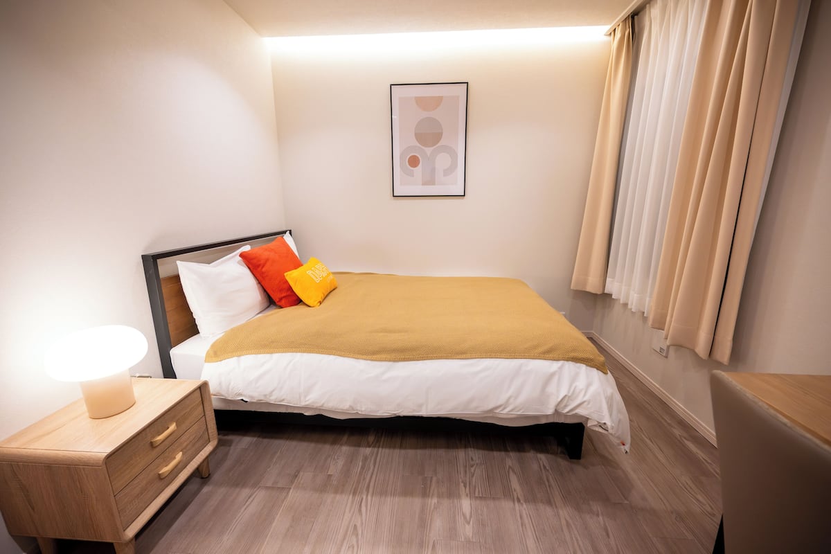 A neatly made bed with a white and yellow bedspread, a wooden nightstand with a lamp, and a framed picture on the wall.
