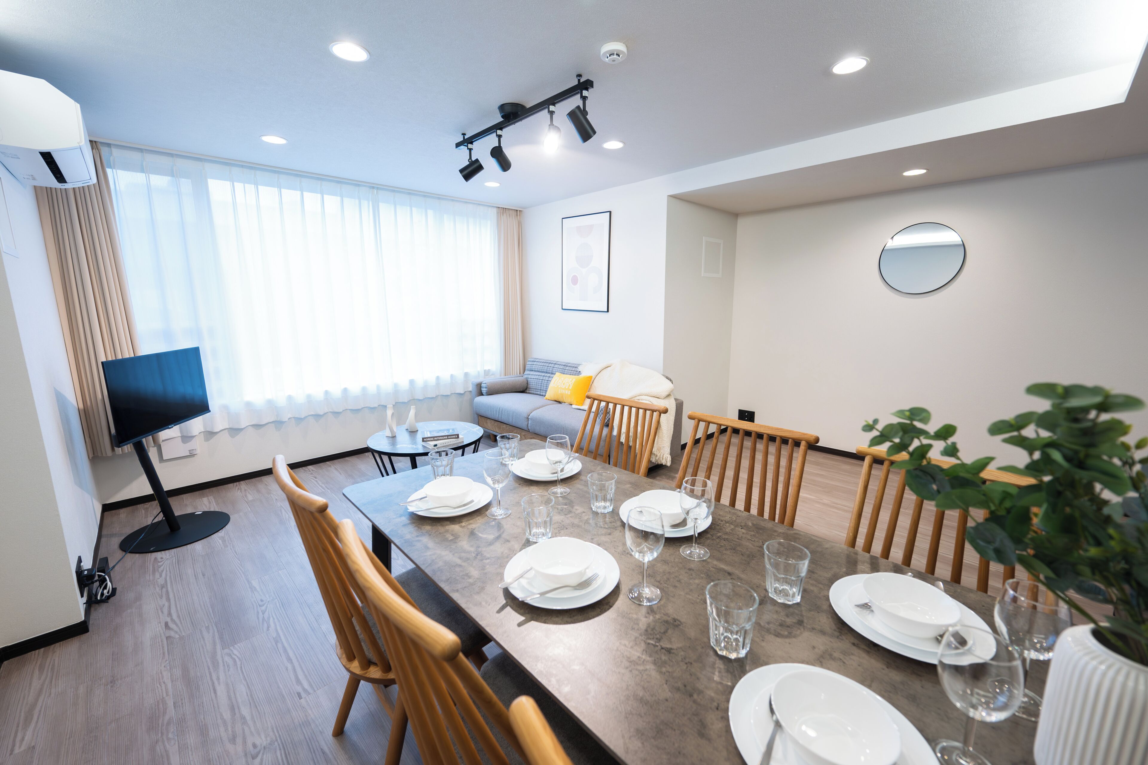 A modern dining area with a long table set for a meal, a television, and a sofa in the background.