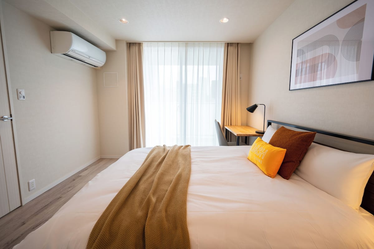 A hotel room with a bed, a desk, an air conditioner, and a framed picture on the wall.