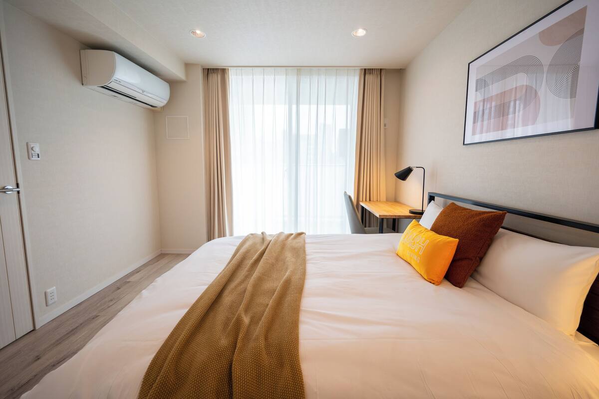 A hotel room with a bed, a desk, an air conditioner, and a framed picture on the wall.