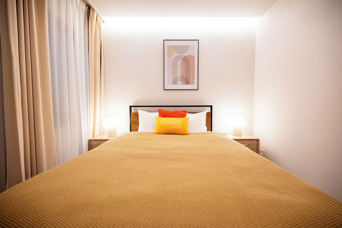 A hotel room with a large bed, a nightstand, a lamp, and a framed picture on the wall.