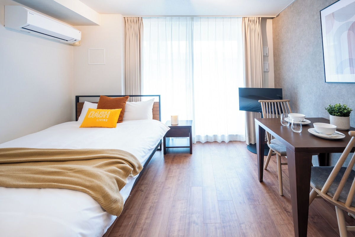 A hotel room with a bed, a desk, a chair, a TV, and a window with curtains.