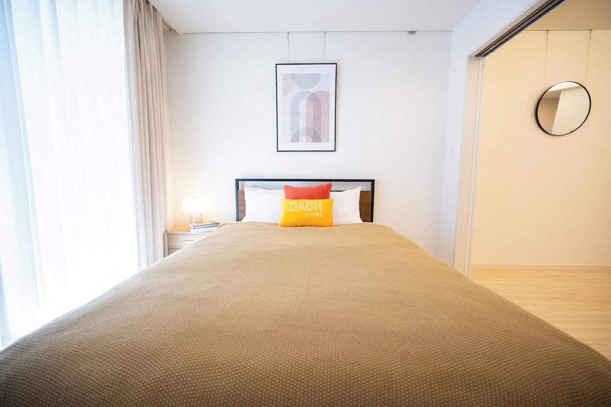 A neatly made bed with a headboard, a framed picture on the wall, and a round mirror on the wall.