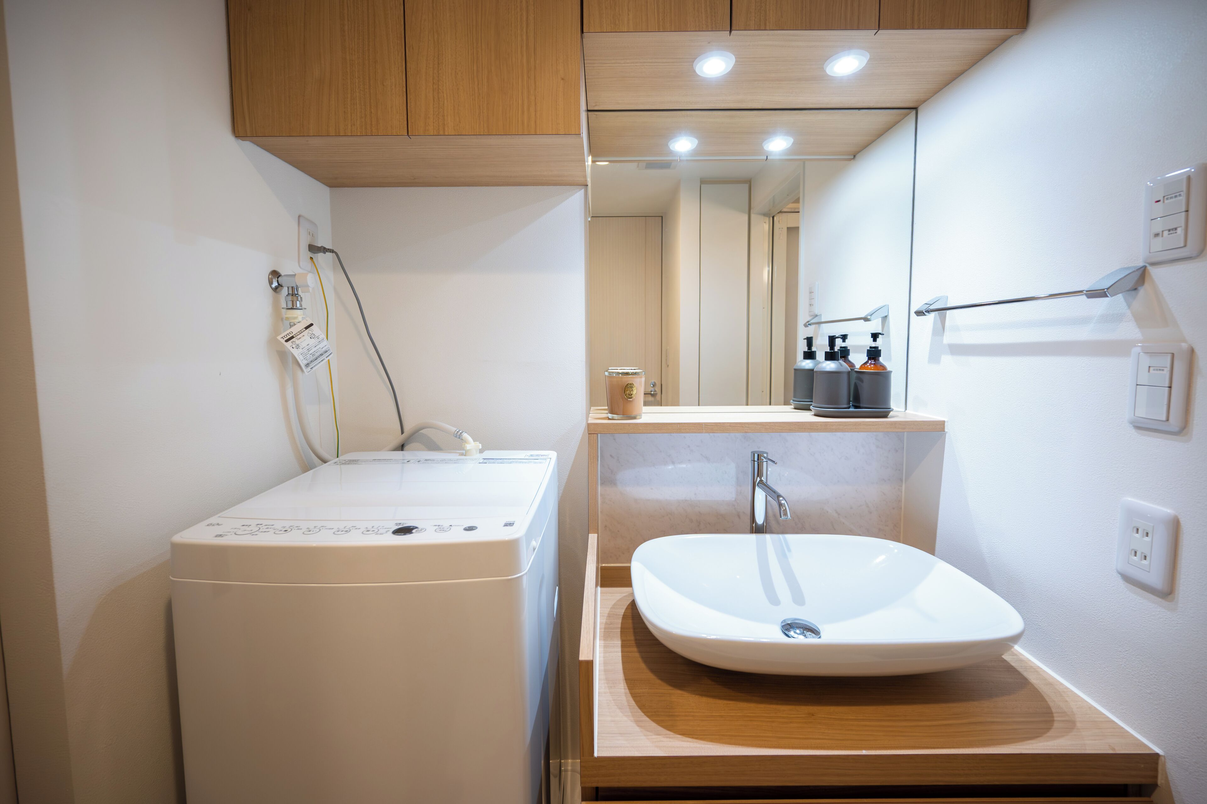 Une salle de bain moderne équipée d’un lave-linge, d’un évier et d’un miroir.