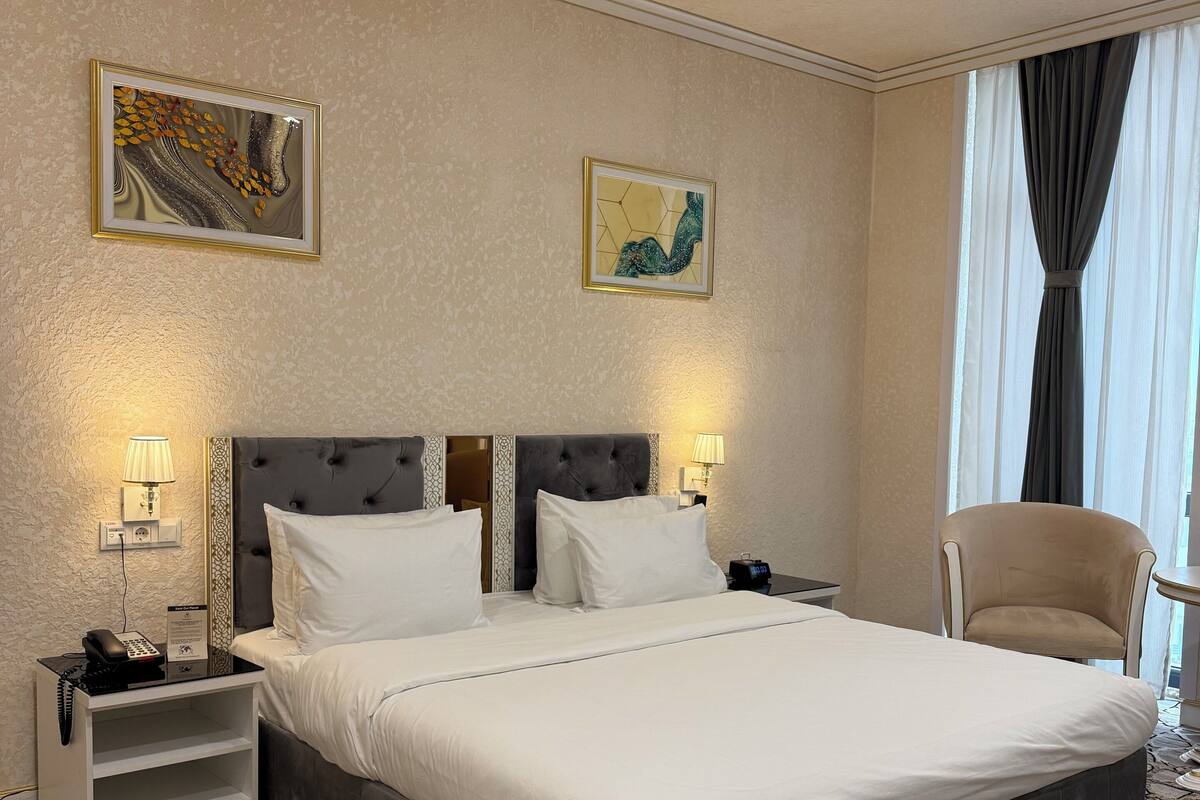 Una camera d'albergo con un letto grande, due comodini con lampade, una sedia e opere d'arte alle pareti.