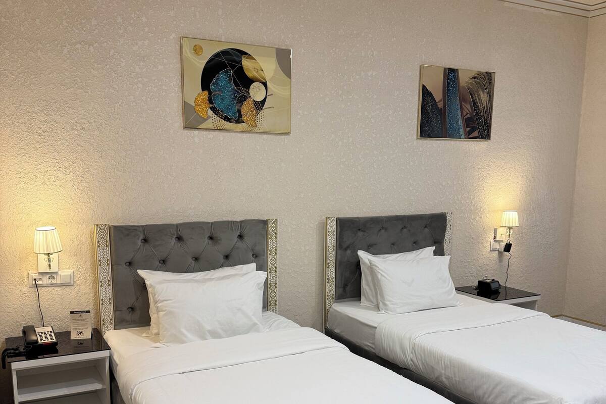 Una camera d'albergo con due letti, un tappeto decorato e opere d'arte alle pareti.