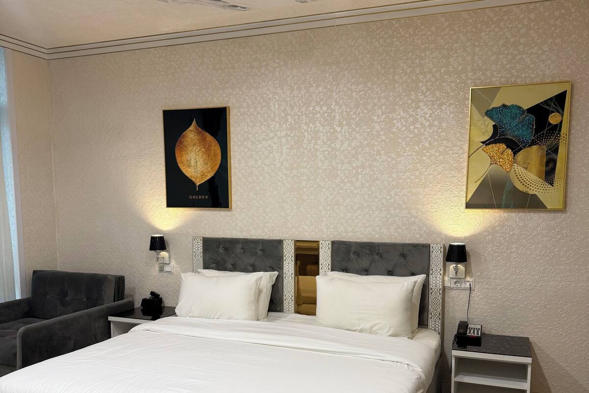 Una camera d'albergo moderna con un letto grande, una poltrona grigia imbottita e un pavimento decorato.