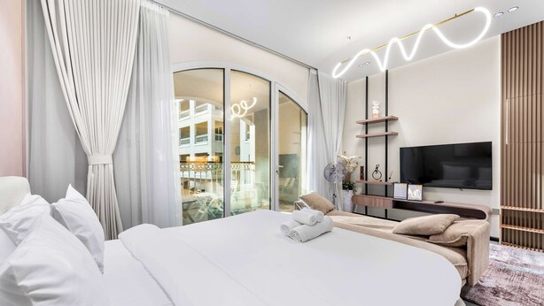 Een moderne slaapkamer met een groot bed, een televisie en een balkon met uitzicht op een gebouw.