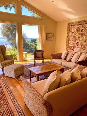 A spacious living room with a large window offering a view of the outdoors, a comfortable sofa, a patterned armchair, and a wooden coffee table.