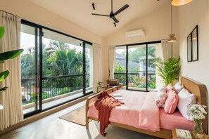 A bedroom with a large window, a bed, a ceiling fan, and a bedside table. - TBK VILLA VAGATOR KOMOREBI 01 (Vagator)