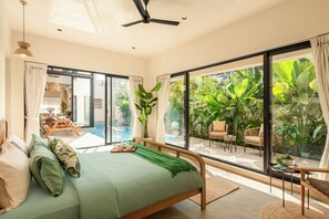A bedroom with a bed, a ceiling fan, and a view of an outdoor pool and tropical plants. - TBK VILLA VAGATOR KOMOREBI 01 (Vagator)